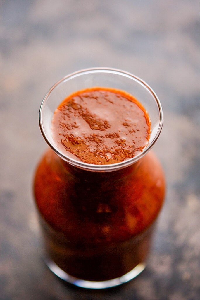 Top view of homemade enchilada sauce in a glass jar on a black background.