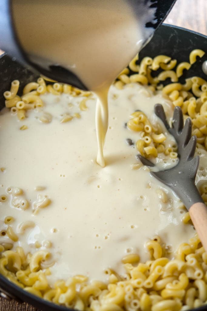 pasta noodles in pan with cheese sauce being poured over