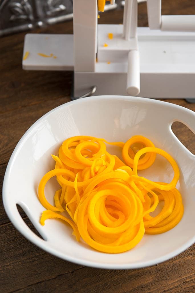 White bowl filled with raw butternut squash noodles with a spiralizer in the background