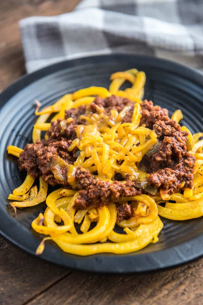 Side angle of Easy Skillet Cincinnati 'Skyline' Chili with Butternut Squash Noodles on a textured black plate with a gray and white checkered napkin