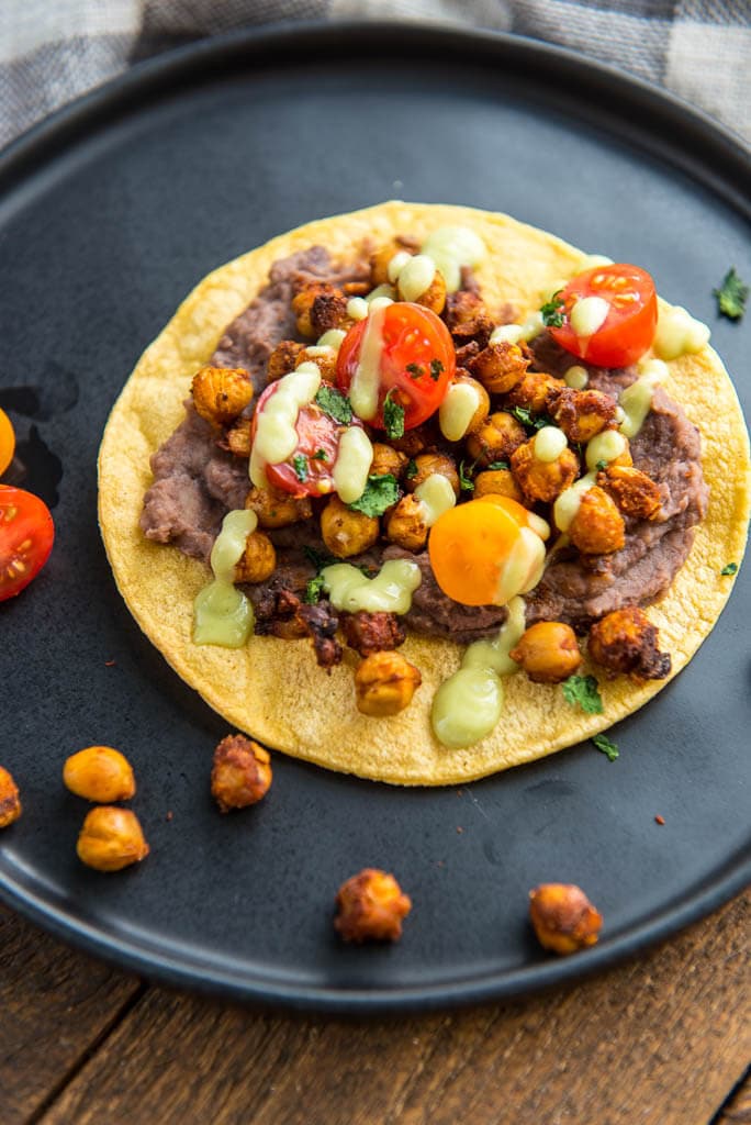 Black Plate with Crispy Chickpea Tostadas and garnished with tomatoes and avocado drizzle