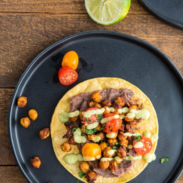 Overhead shot of limes plus Black Plate with Crispy Chickpea Tostadas and garnished with tomatoes and avocado drizzle