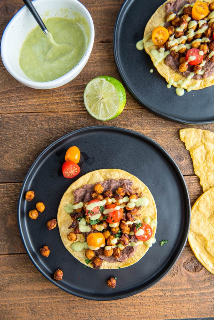 Overhead shot of two Black Plates with Crispy Chickpea Tostadas and garnished with tomatoes and avocado drizzle