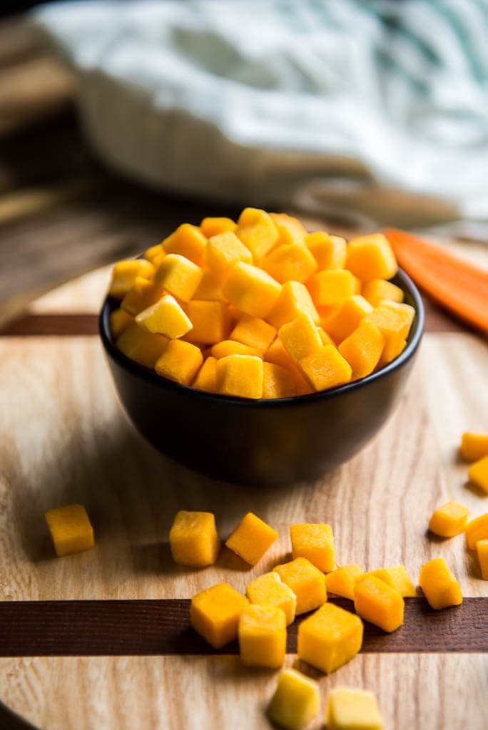 Small black bowl filled with cubed butternut squash on cutting board for Butternut Squash Minestrone