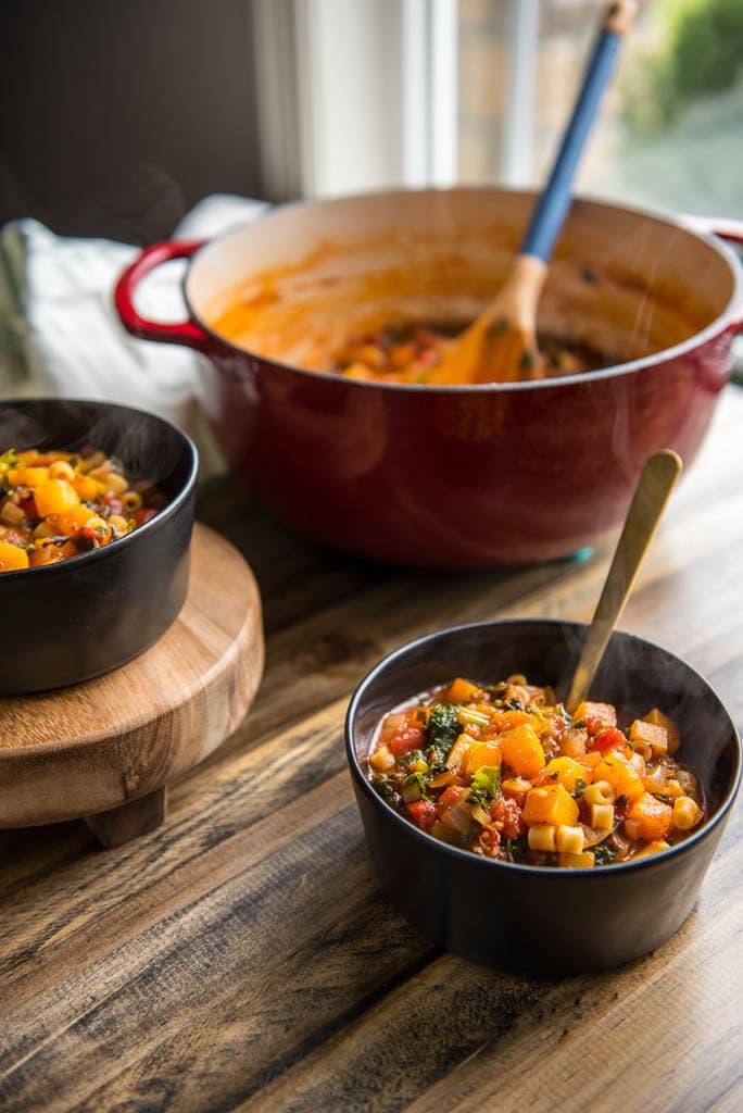 Table setting with Butternut Squash Minestrone in black bowls with a red dutch oven in background.