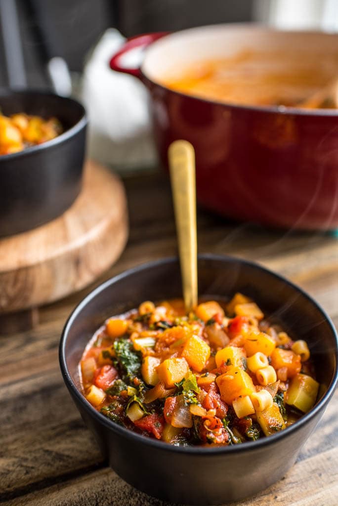 Table setting with Butternut Squash Minestrone in black bowls with a red dutch oven in background.