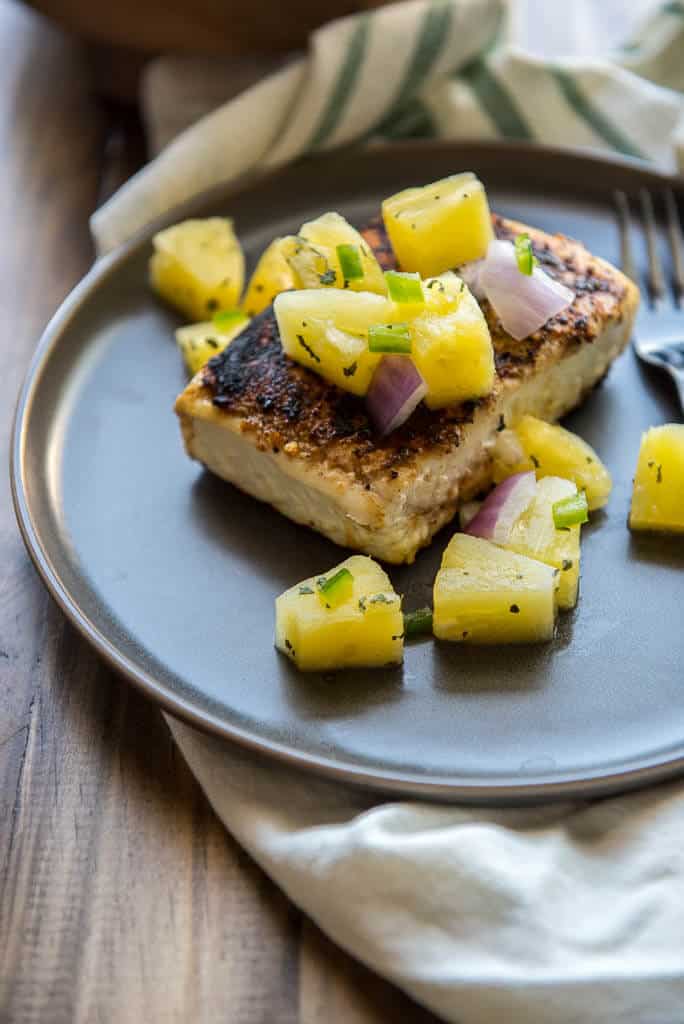 Pan Seared Halibut Recipe with Pineapple Salsa on gray plate with white and green napkin on wood table.