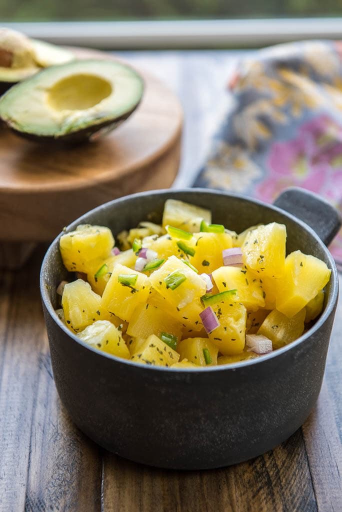 Fresh pineapple salsa in a metal bowl in front of avocado and a floral napkin for Shrimp Tacos in a Bowl with Pineapple Salsa.