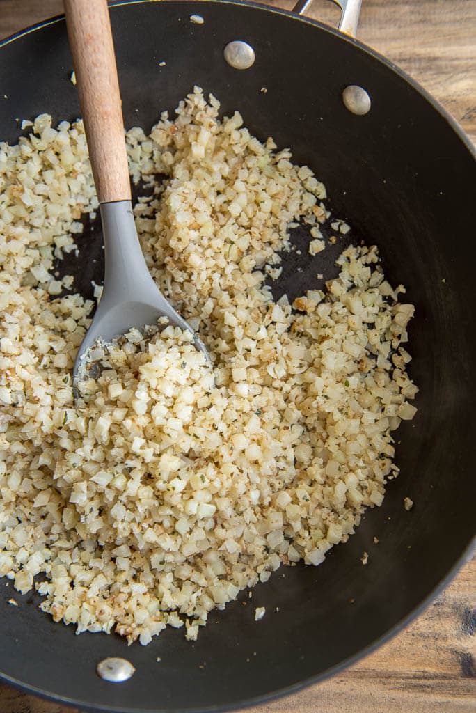 Overhead shot of cauliflower rice with wooden spoon cooked in a skillet for Shrimp Tacos in a Bowl with Pineapple Salsa.