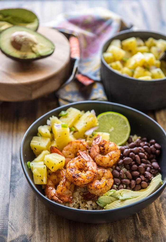 A black bowl filled with Shrimp Tacos in a Bowl with Pineapple Salsa, avocado, black beans and lime.