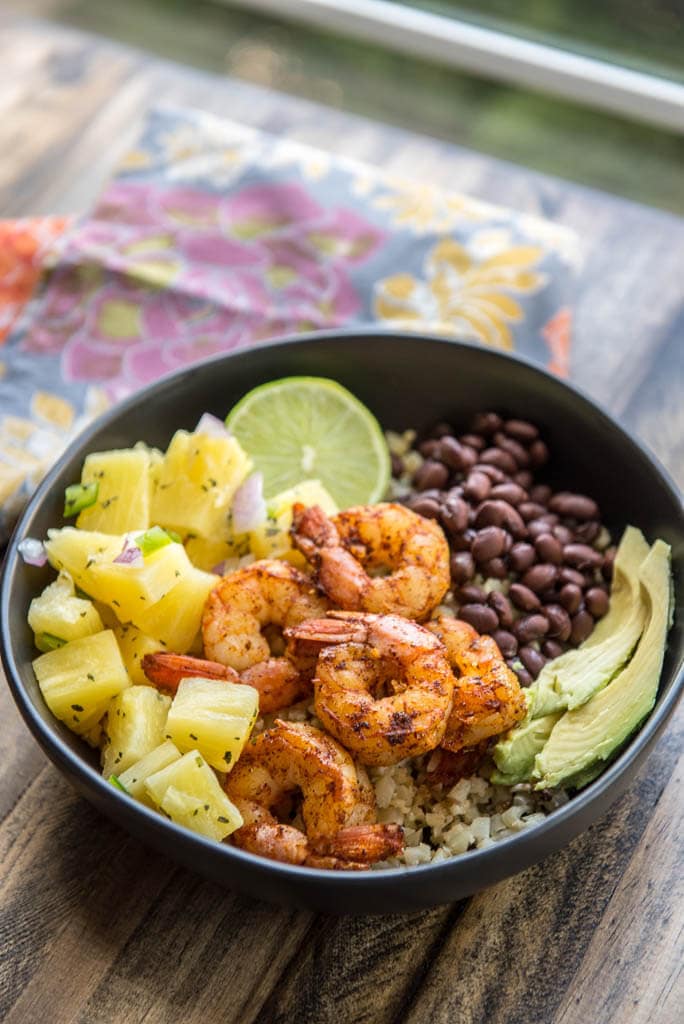 Black bowl and floral napkin with Shrimp Tacos in a Bowl with Pineapple Salsa plus black beans and avocado.