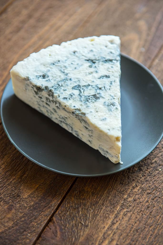 A wedge of gorgonzola cheese and a gray plate for Wedge Salad with Herbed Buttermilk Dressing.