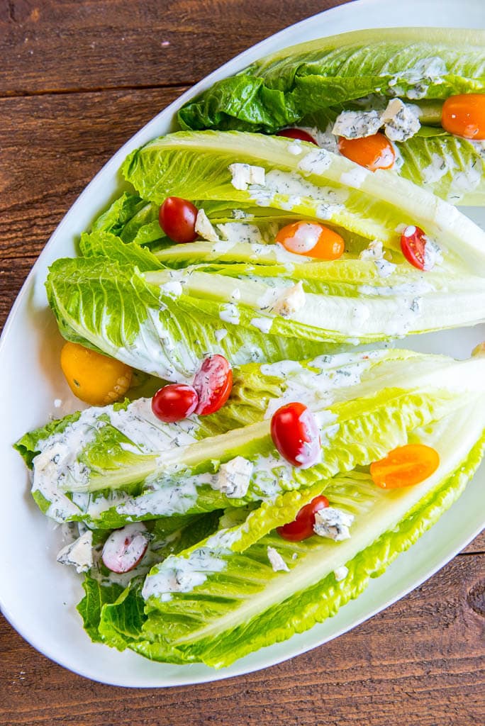Romaine wedge salad with tomatoes and herbed buttermilk dressing on a white platter.