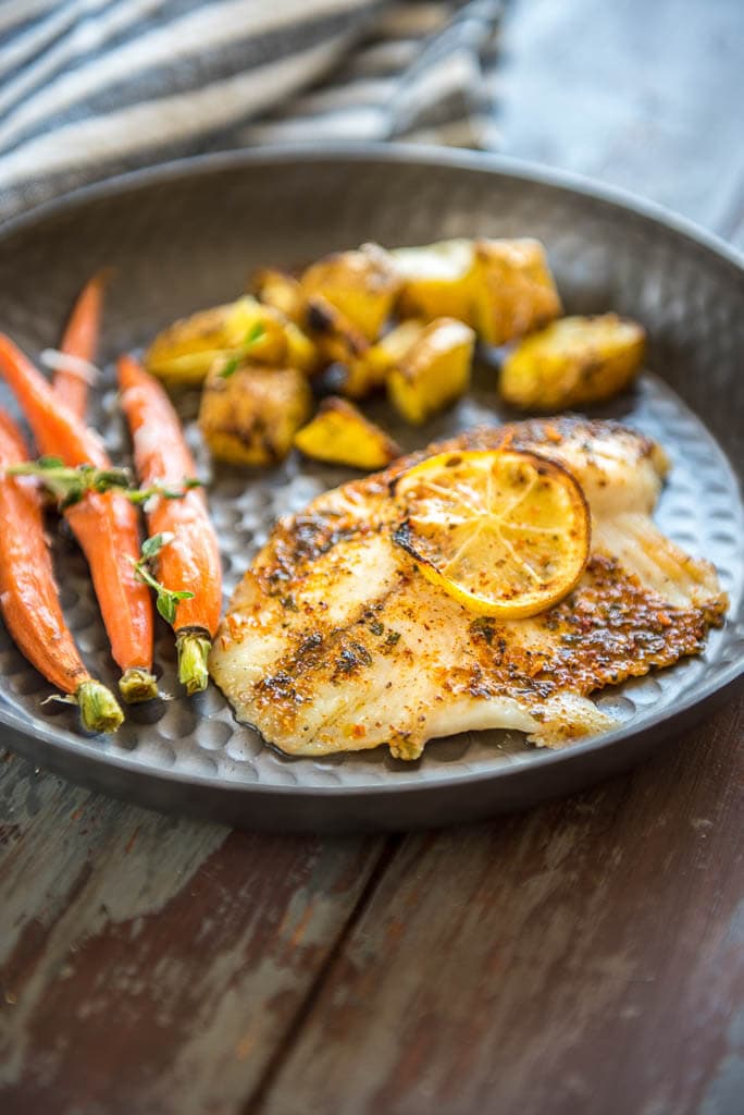 Baked Lemon Butter Tilapia on metal plate served with potatoes and carrots