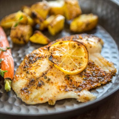 Baked Lemon Butter Tilapia on metal plate served with potatoes and carrots