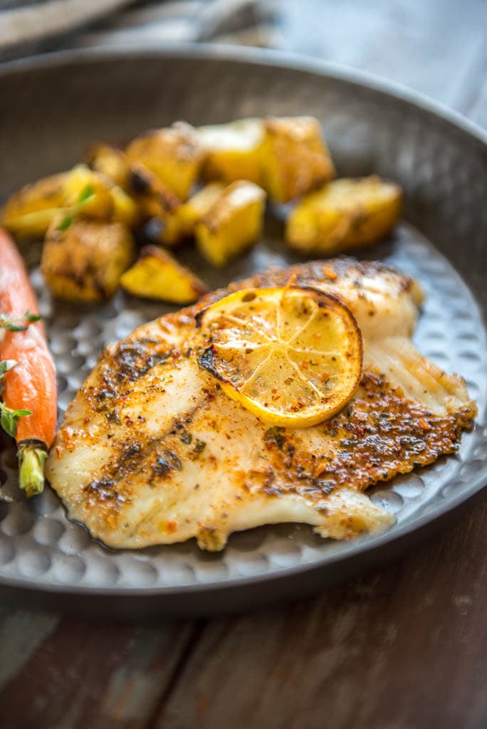 Baked Lemon Butter Tilapia on metal plate served with potatoes and carrots