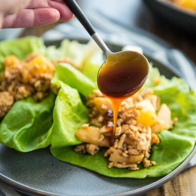 Chicken Lettuce Wraps on black plate with sauce being drizzled from spoon