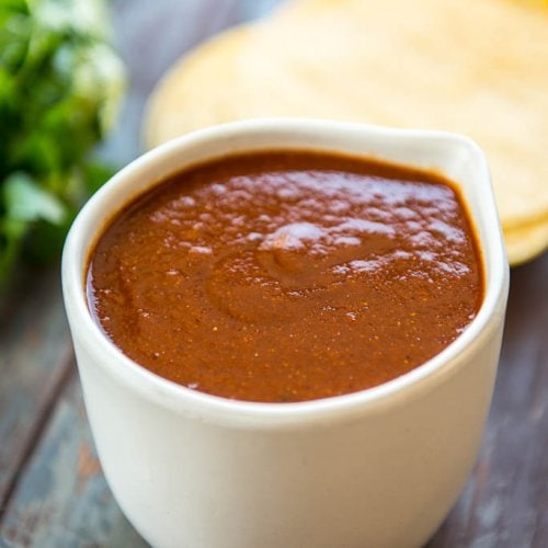 Homemade Enchilada Sauce in white bowl on wood table with tortillas
