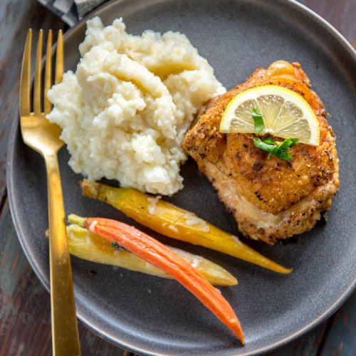 Crispy Lemon Pepper Chicken Thigh on gray plate with carrots and mashed cauliflower