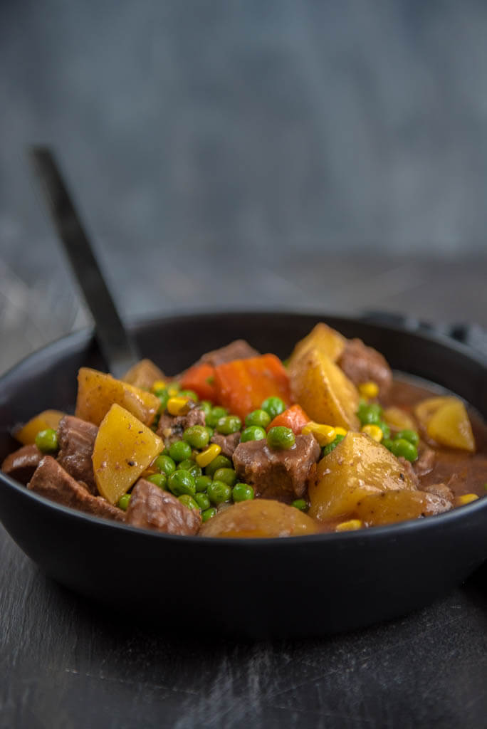 Slow Cooker Beef Stew in Black Bowl with Black Spoon