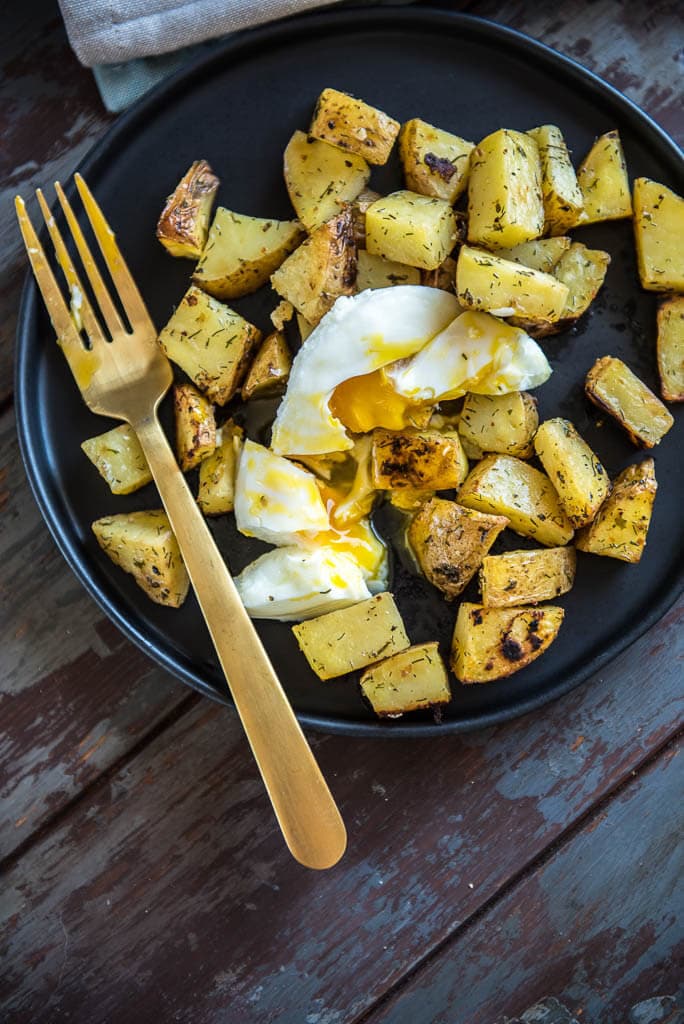 Easy Weekday Breakfast Potatoes on a black plate topped with a poached egg