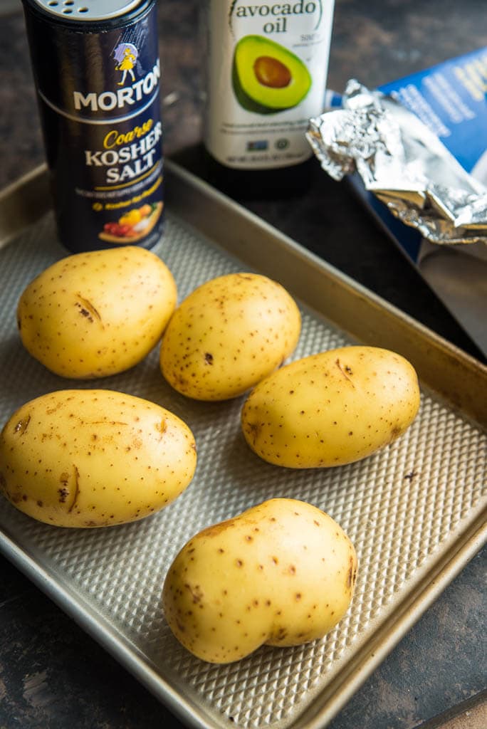 5 potatoes on a baking sheet ready to coat with olive oil and kosher salt