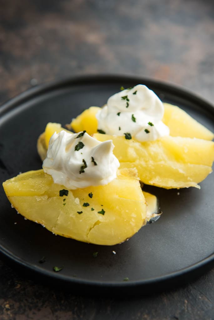 baked potato cut in half topped with sour cream and chives on black plate