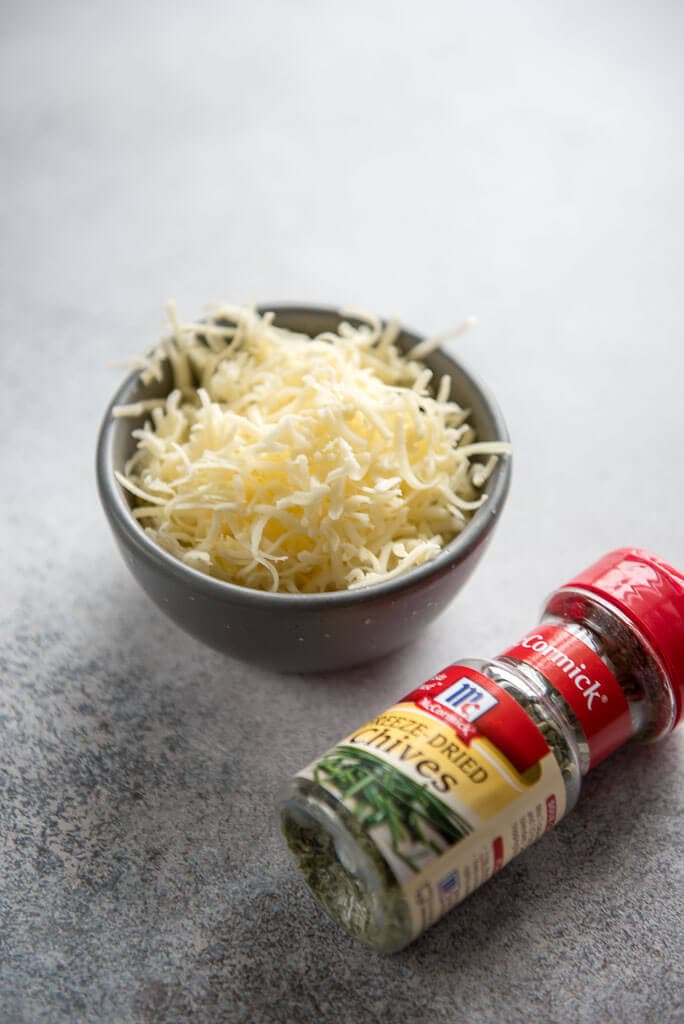 shredded white cheese in gray bowl next to jar of chives for Instant Pot Sous Vide Egg Bites