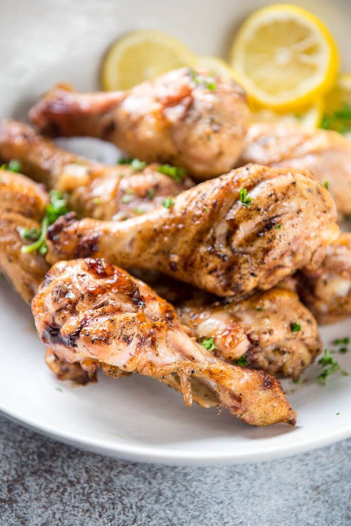 Lemon Herb Grilled Chicken Drumsticks on a white platter with fresh lemon slices