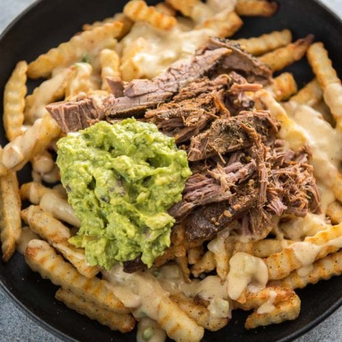 carne asada fries topped with guacamole in a cast iron skillet