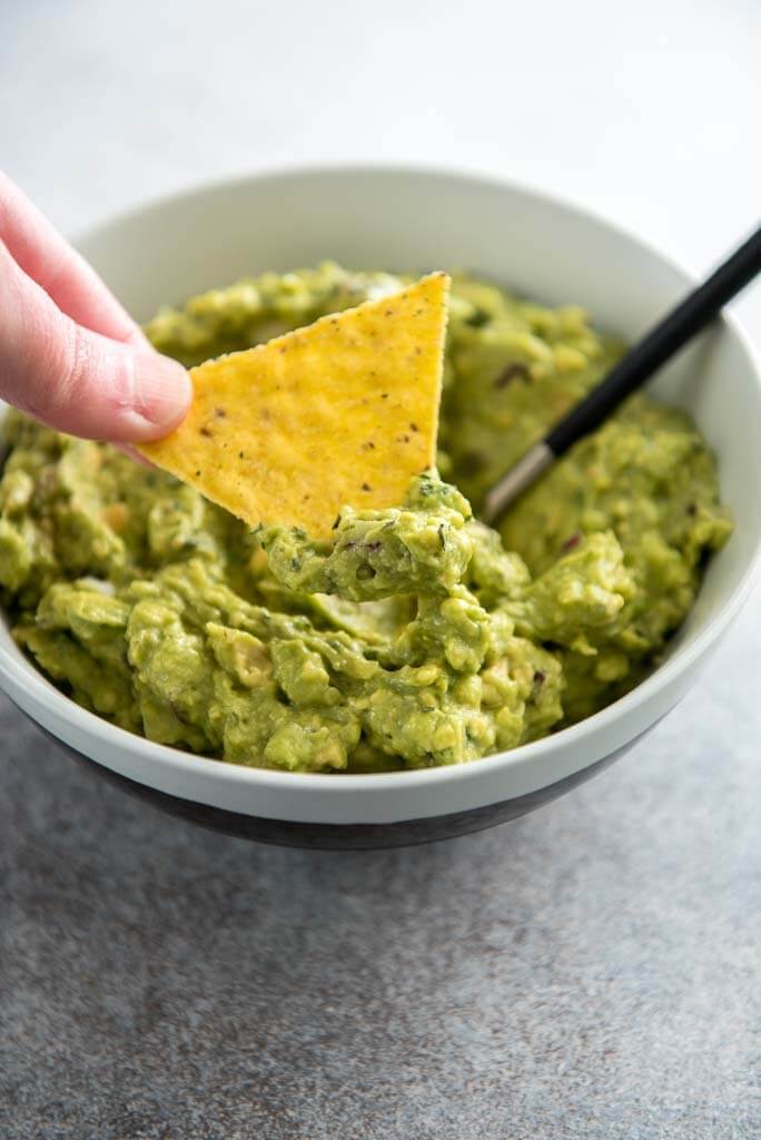 chip being dipped into guacamole in a white bowl