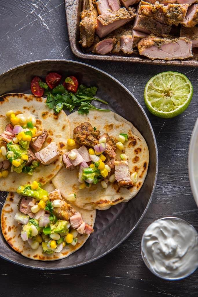 chicken street tacos on metal plate topped with avocado corn salsa