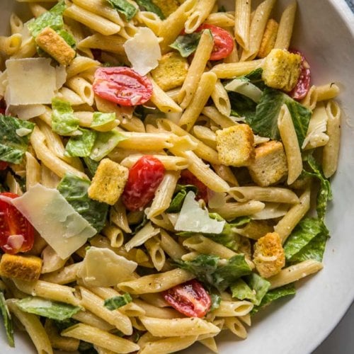 Caesar Pasta Salad in a white bowl topped with shaved parmesan cheese