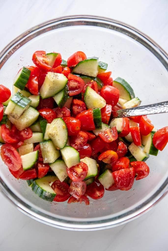 cucumber tomato salad being mixed in a glass bowl