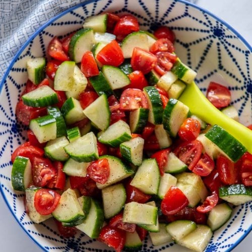 cucumber tomato salad in a blue and white serving bowl with a green spoon