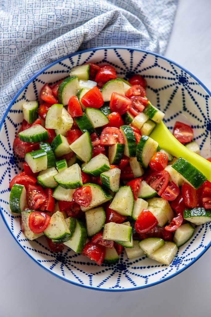 cucumber tomato salad in a blue and white serving bowl with a green spoon