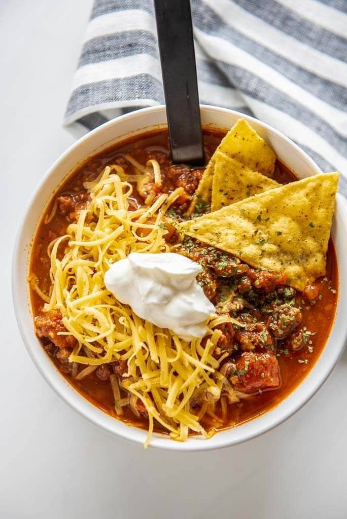 white bowl full of healthy chili topped with chips, cheese and sour cream
