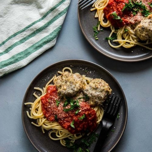 turkey meatballs on top of spaghetti with marinara on gray plates topped with cheese and parsley