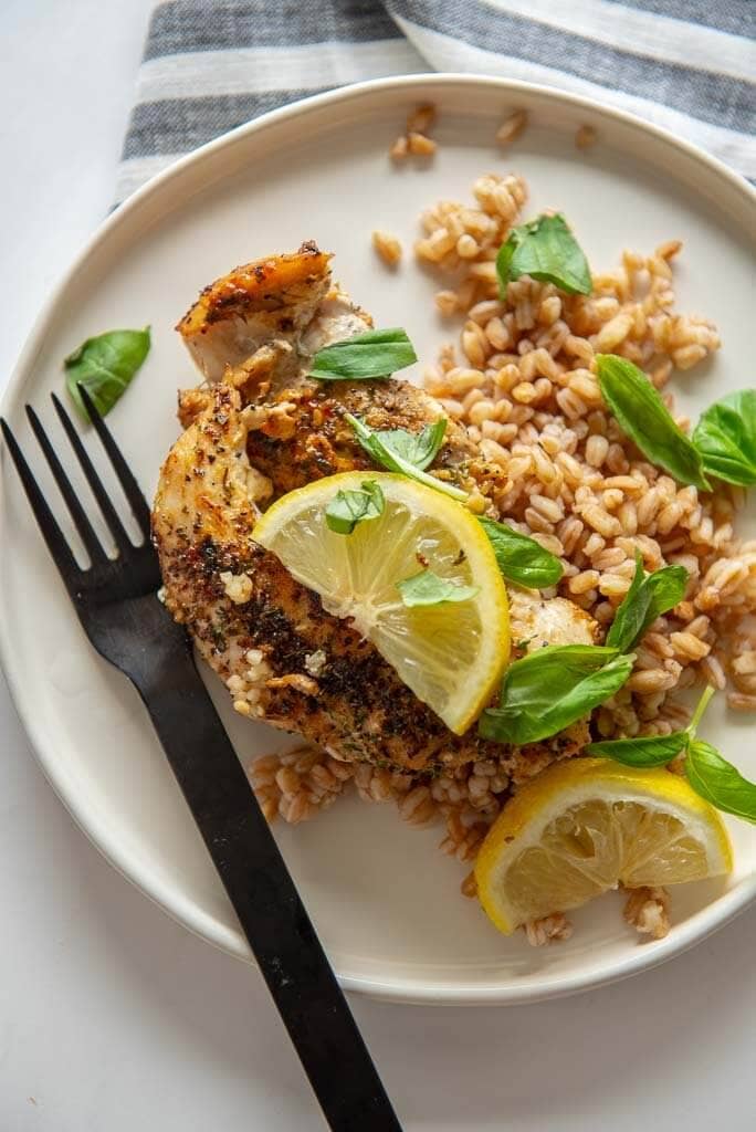 lemon basil chicken with farro on white plate topped with lemon slices and basil