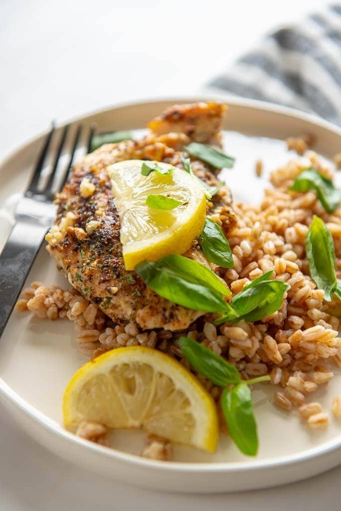 lemon basil chicken with farro on white plate topped with lemon slices and basil