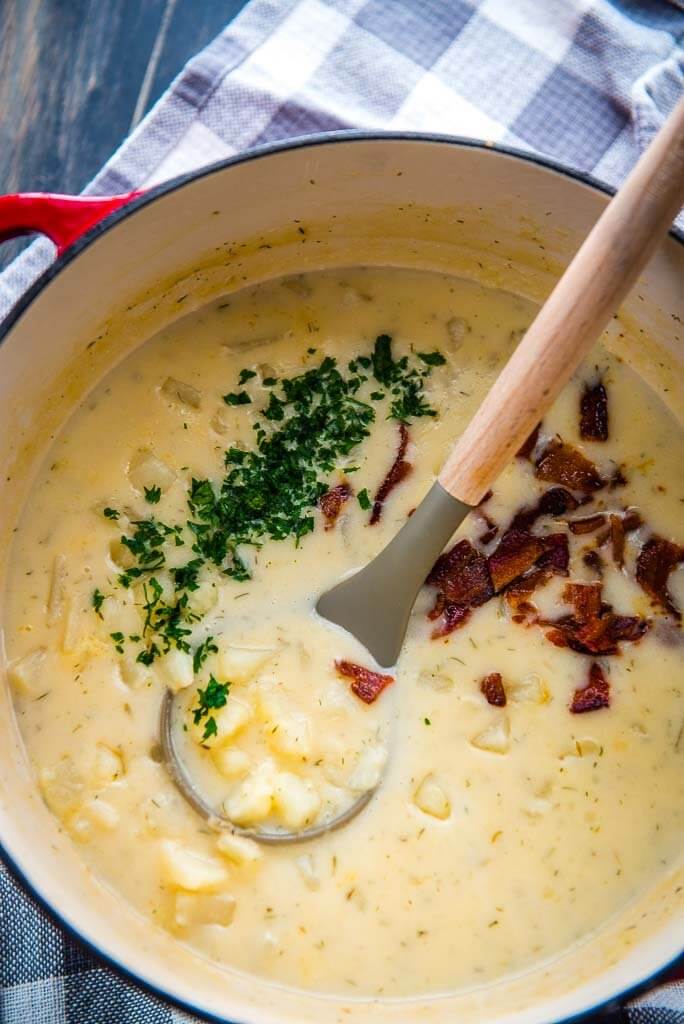 creamy potato soup in a red and white cast iron pot topped with bacon and parsely