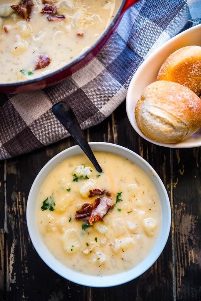 white bowl filled with creamy potato soup topped with bacon with a side of rolls