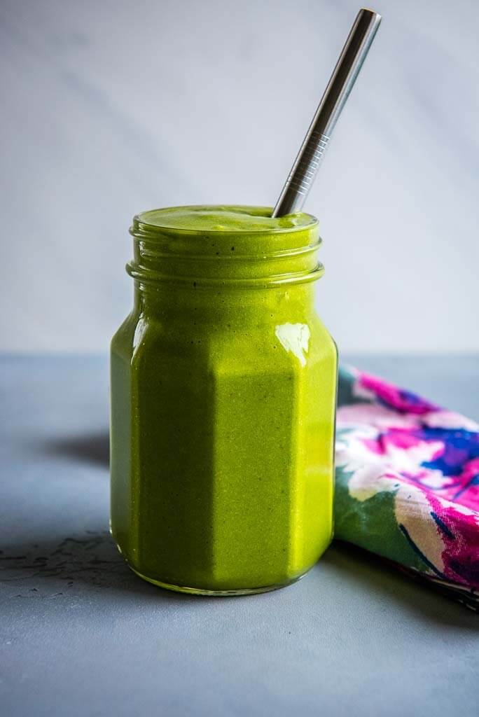 Mango Spinach Smoothie in glass mason jar with colorful napkin and metal straw