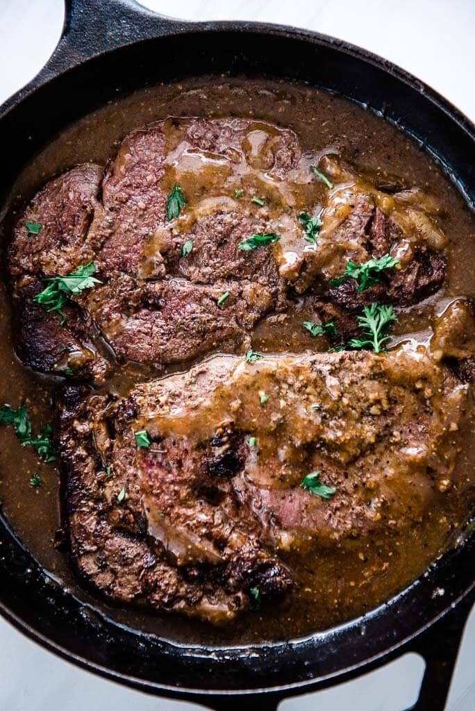 skillet steak with gravy in cast iron skillet topped with parsley