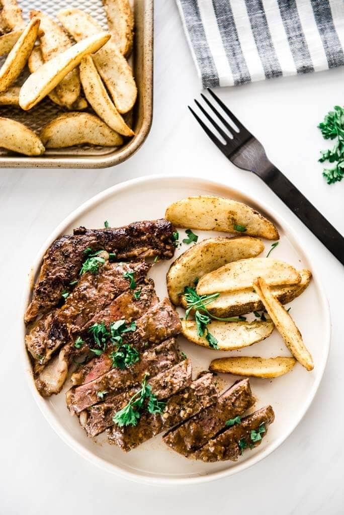 sliced skillet steak on white plate with oven fries