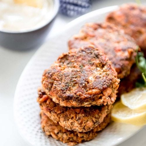 6 fresh salmon patties on white oval platter with a side of mayo and lemon