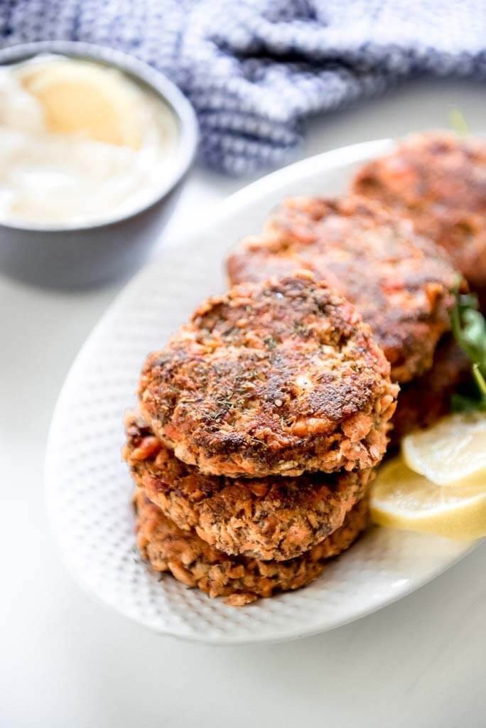 6 fresh salmon patties on white oval platter with a side of mayo and lemon
