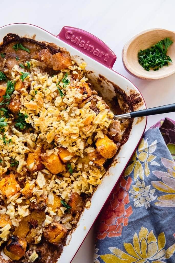 savory butternut squash casserole in a red casserole dish with a fall napkin and topped with parsley 