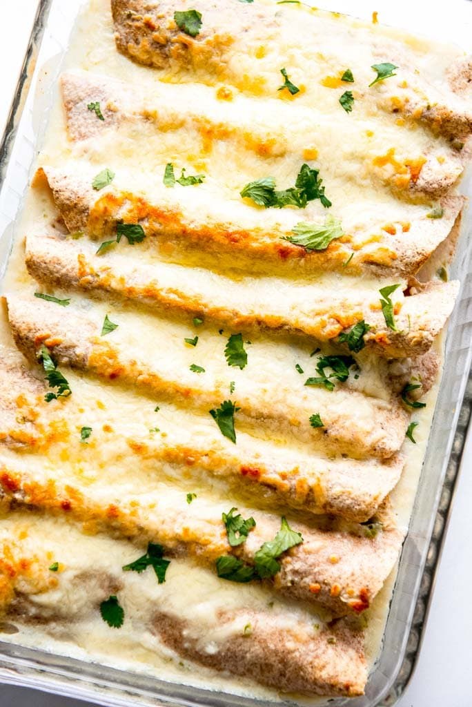 casserole dish with baked chicken enchiladas with white sauce topped with cilantro