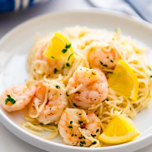 lemon garlic shrimp pasta on a white plate with lemon slices